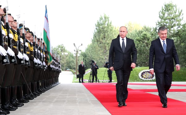 Vladimir Putin and Uzbek leader Shavkat Mirziyoyev walk along a red carpet past an Uzbek honour guard